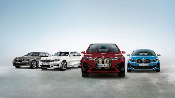 Vier BMW-Autos in verschiedenen Farben stehen nebeneinander auf grauem Boden vor blauem Himmel.