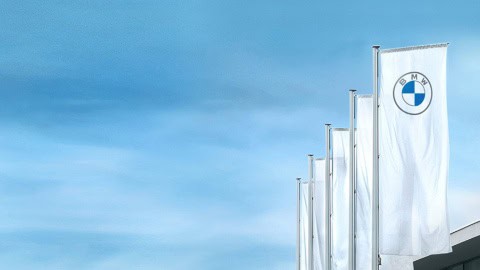 Weiße BMW-Flaggen wehen an Masten vor blauem Himmel.