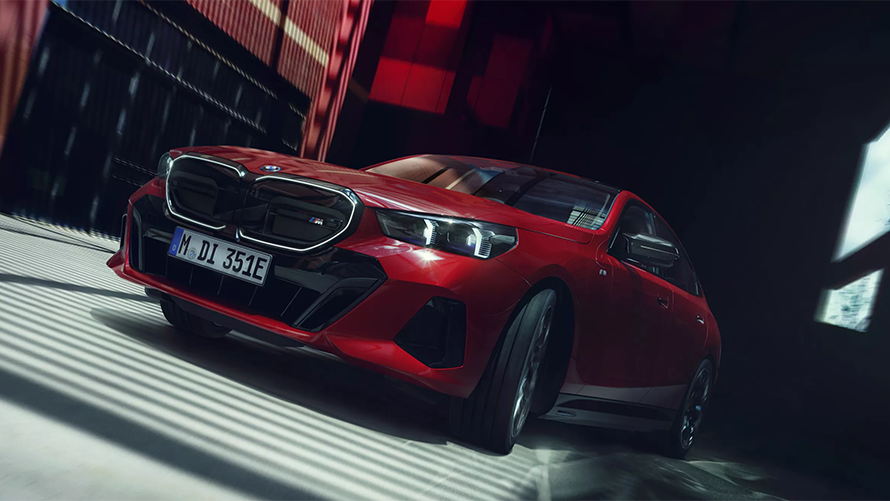 Roter BMW i5 M60 vor dunklem Hintergrund, schräg von vorne fotografiert.