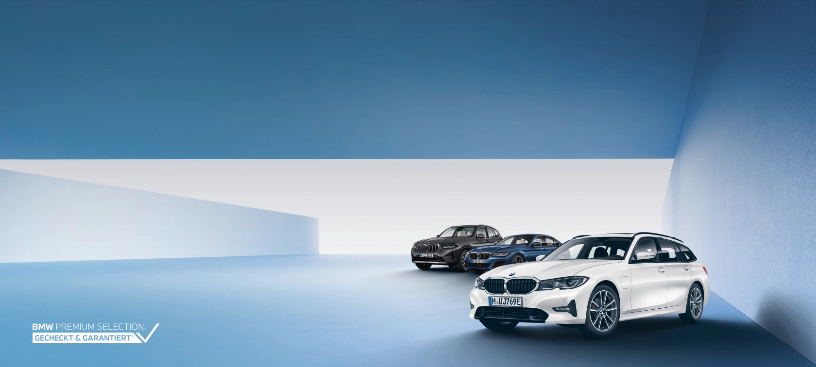 Drei BMW-Modelle in einem blauen Raum, vorne ein weißer BMW, hinten zwei dunklere Modelle.