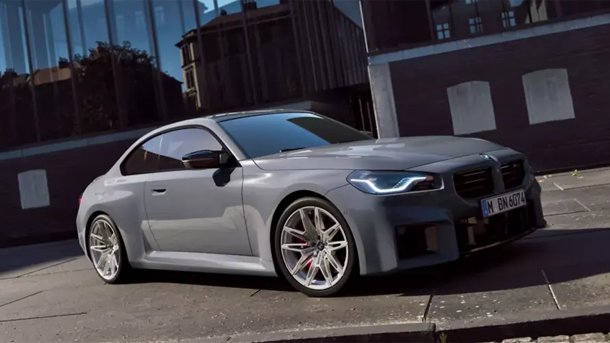 Graues BMW 2er M Coupé auf einer Straße vor einem modernen Gebäude.