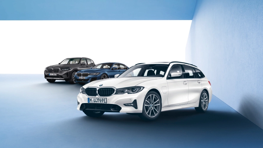 Drei BMW-Fahrzeuge in einem hellblauen Raum, im Vordergrund ein weißer Kombi.