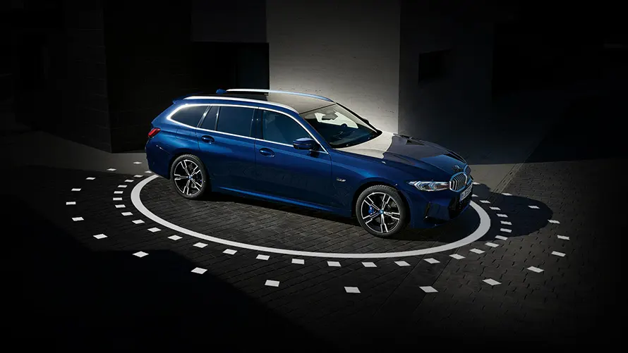 Blauer BMW Kombi auf gepflastertem Boden, von Licht umgeben, in dunkler Umgebung.