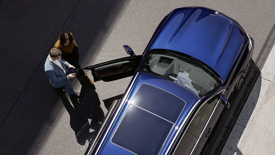 Zwei Personen neben einem blauen Auto auf der Straße, fotografiert von oben.