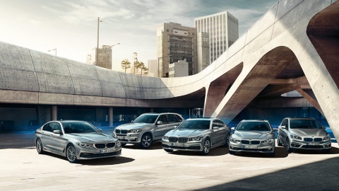 Fünf silberne BMW-Modelle stehen nebeneinander vor moderner Architektur im Freien.