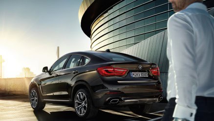 Ein schwarzer BMW vor einem modernen Gebäude bei Sonnenuntergang, Person im Vordergrund.