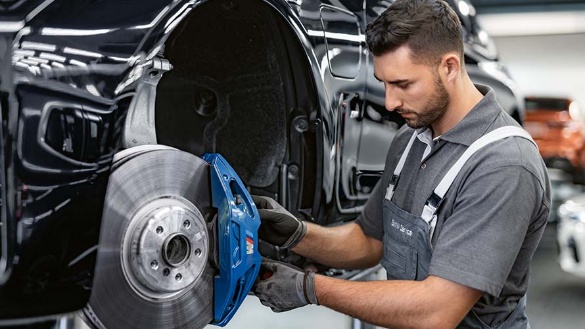 Mechaniker arbeitet an einer blauen Bremse eines Autos in einer Werkstatt.