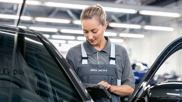 Eine Mechanikerin in BMW-Uniform arbeitet an einem schwarzen Auto in einer Werkstatt.