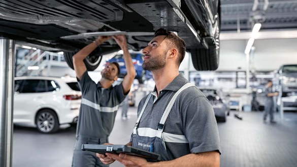 Zwei Mechaniker arbeiten in einer Werkstatt an einem angehobenen Auto.