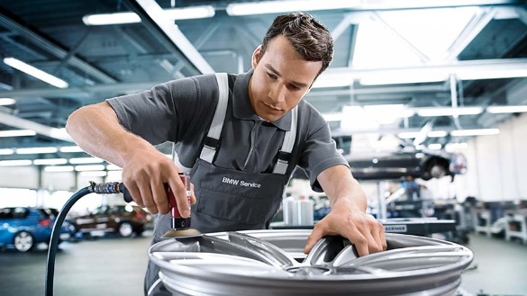 Mechaniker bearbeitet eine silberne BMW-Felge in einer Werkstatt.