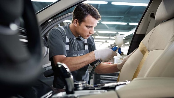 Ein Mechaniker repariert den beigen Fahrzeugsitz im Innenraum eines BMW.