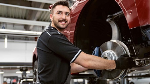 Mechaniker wechselt Bremsscheibe an rotem Auto in Werkstatt.