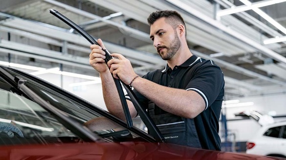 Mechaniker wechselt Scheibenwischer an rotem Auto in Werkstatt.