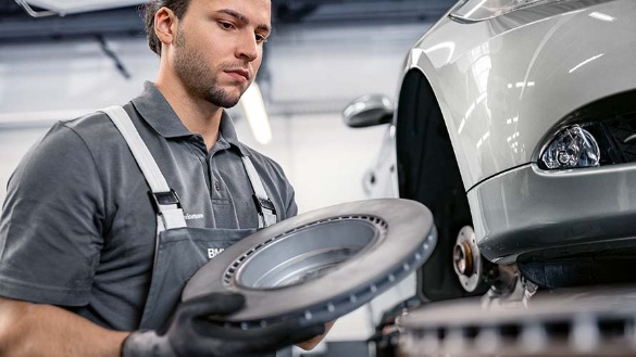 Ein Mechaniker hält eine Bremsscheibe neben einem angehobenen Auto in einer Werkstatt.