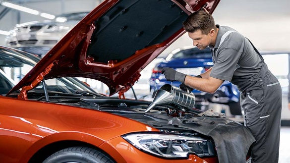 Ein Mechaniker füllt Öl in einen roten BMW mit geöffneter Motorhaube in einer Werkstatt.
