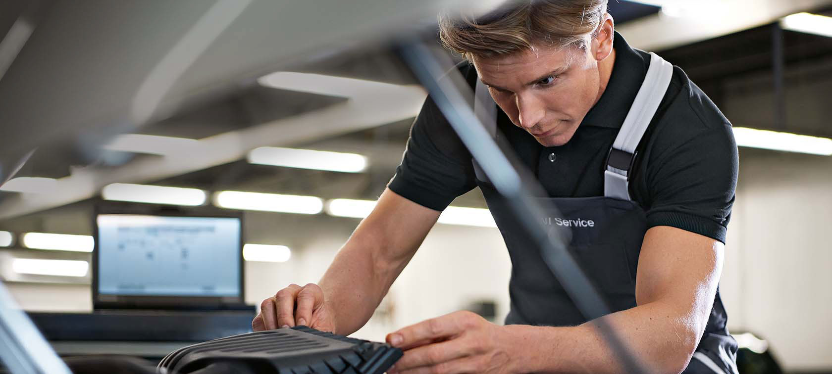 Mechaniker in schwarzer Arbeitskleidung arbeitet konzentriert an einem Fahrzeug in einer Werkstatt.