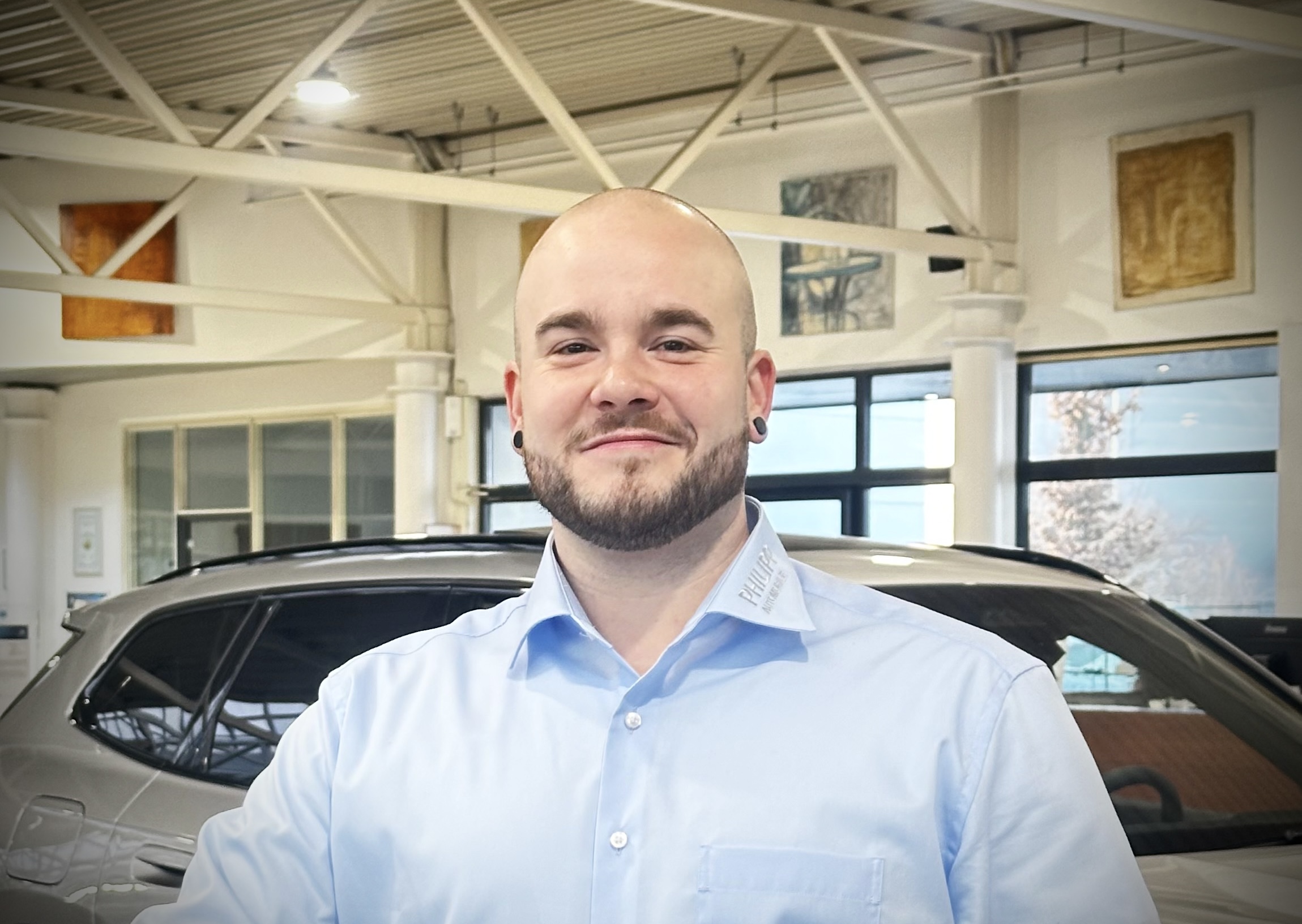 Mann in blauem Hemd in einem Autohaus, im Hintergrund ein graues Auto.