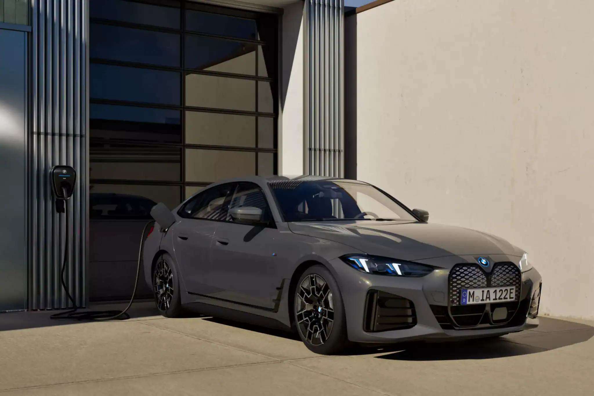 Grauer BMW i4 lädt an einer Ladestation vor einem modernen Gebäude.