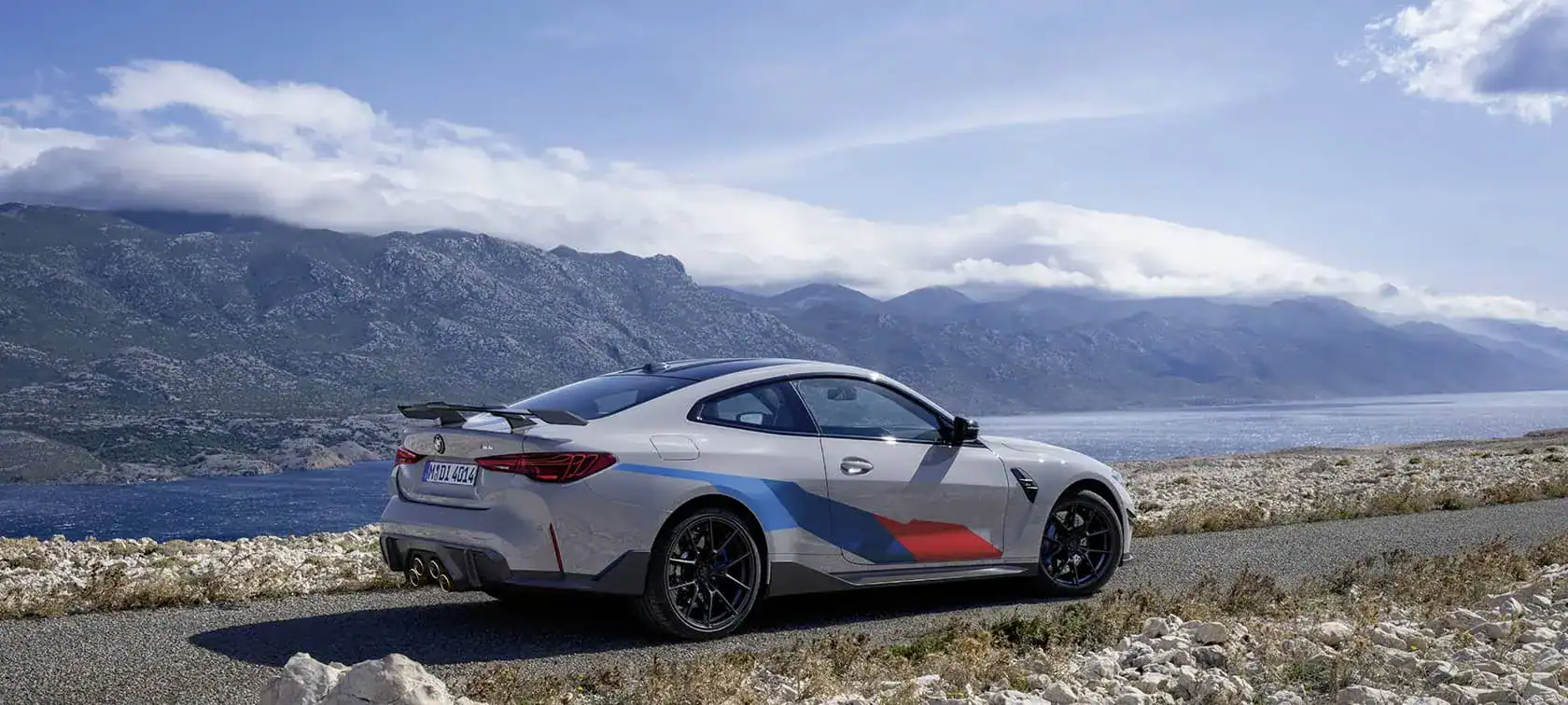 Silberner BMW auf Küstenstraße, im Hintergrund Berge und Meer unter blauem Himmel.