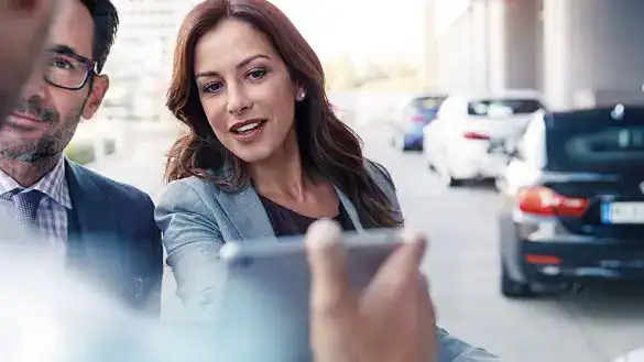 Zwei Personen betrachten ein Tablet, im Hintergrund parken Autos auf einer Straße.