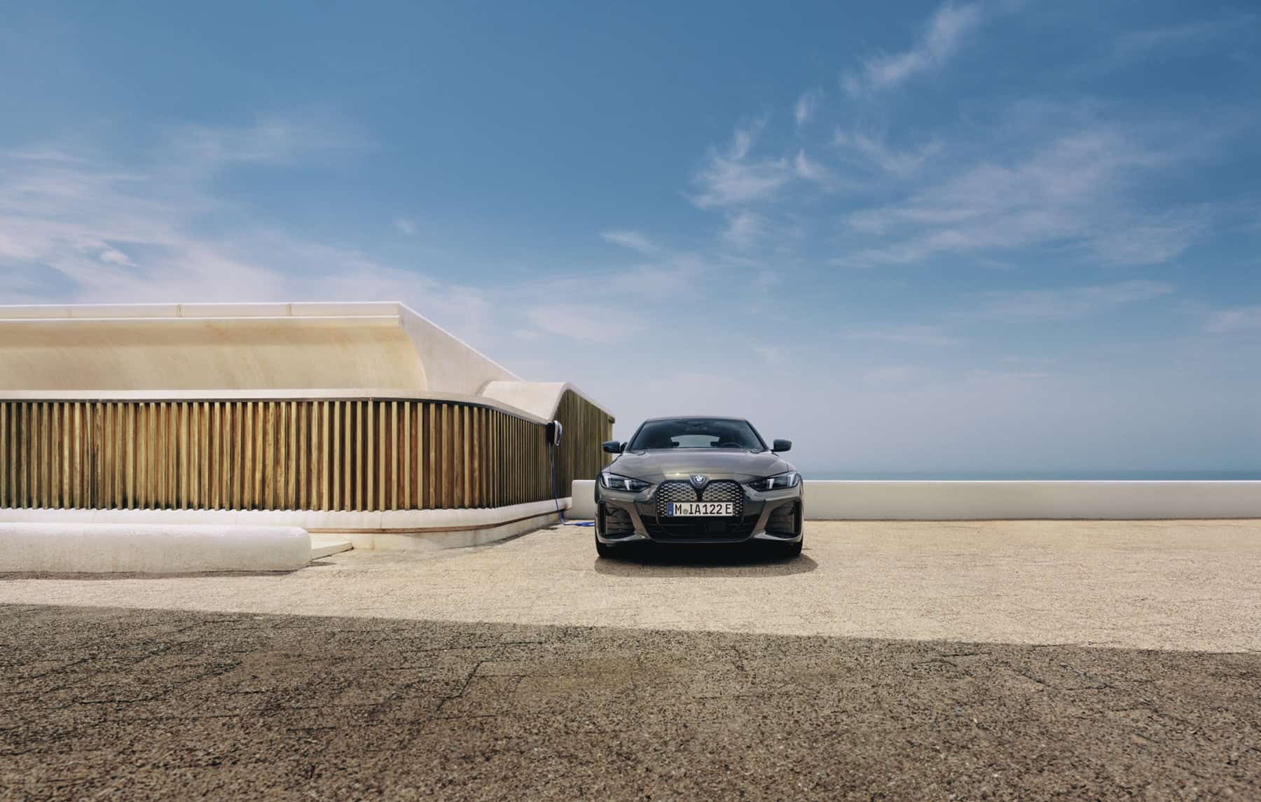 BMW i4 in grau auf einem Parkplatz vor einem modernen Gebäude, blauer Himmel im Hintergrund.