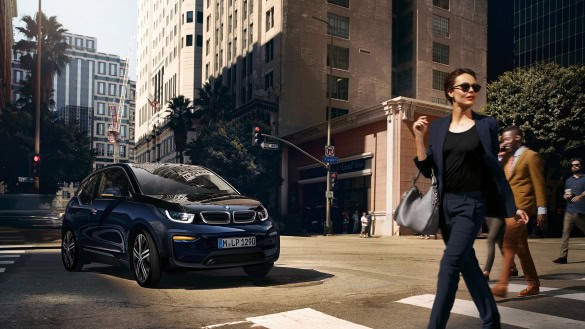 Eine Frau überquert eine Straße, während ein BMW i3 in einer Stadt fährt.