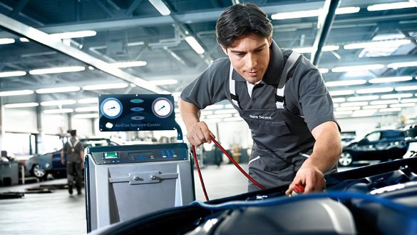 Mechaniker überprüft Klimaanlage eines Fahrzeugs in einer Werkstatt mit Diagnosegerät.